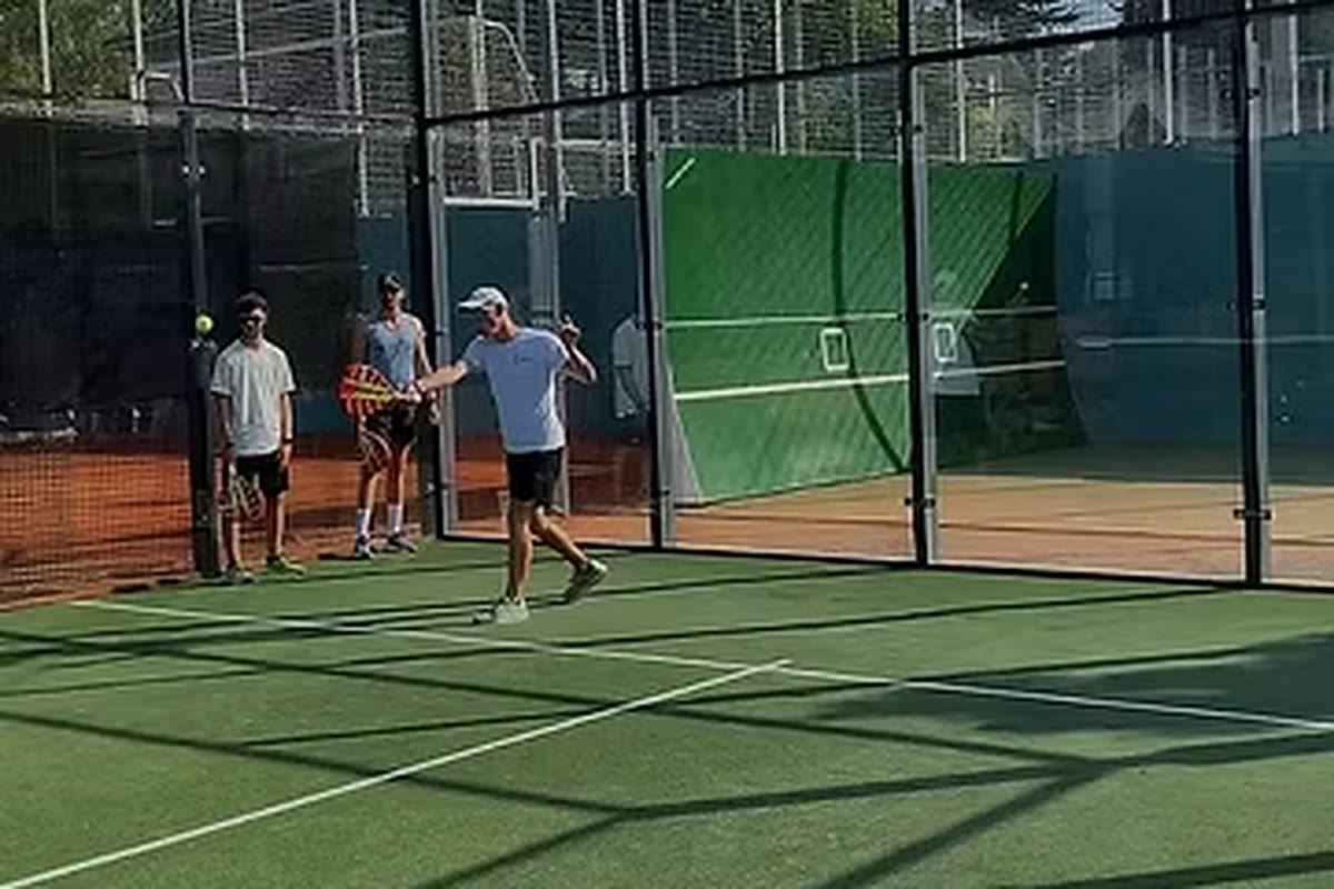 Padel-Spieler holt auf einem Outdoor-Padelplatz zum Schlag aus, ein Ball fliegt über das Netz